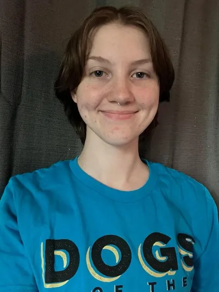 Marisa Kaiser is both pet CPR certified and a pet professional guild member; speaking volumes to her dedication to her clients at Dogs of the Dunes. Her blue Dogs of the Dunes shirt is visible. She is an expert in working with all types of dogs, including those with behavioral issues, and uses positive reinforcement meaning you get affordable dog training that works.